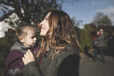 Smiling mother carrying daughter outdoors - KMKF00839