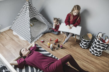 Mutter entspannt sich mit zwei Mädchen im Kinderzimmer zu Hause - KMKF00844