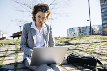 Businesswoman in the city, sitting on ground, working on laptop - JRFF03022