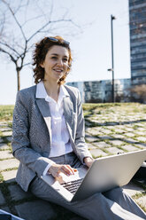 Geschäftsfrau in der Stadt, auf dem Boden sitzend, am Laptop arbeitend - JRFF03024