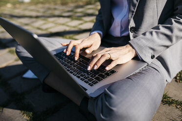 Businesswoman in the city, sitting on ground, working on laptop - JRFF03026