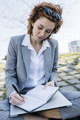 Geschäftsfrau in der Stadt, auf dem Boden sitzend, in ein Notizbuch schreibend - JRFF03030