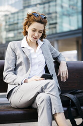 Young businesswoman sitting on a bench in the city, using smartphone - JRFF03050