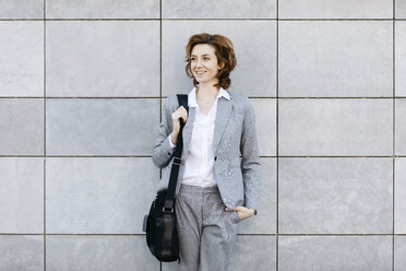 Porträt einer jungen selbstbewussten Geschäftsfrau vor einer Wand mit grauen Fliesen - JRFF03062