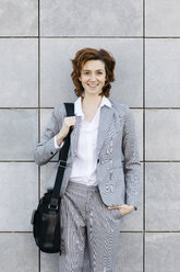 Portrait of a young confident businesswoman in front of wall with gray tiles - JRFF03063