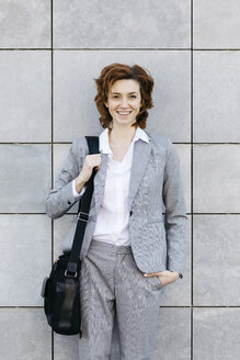 Porträt einer jungen selbstbewussten Geschäftsfrau vor einer Wand mit grauen Fliesen - JRFF03063