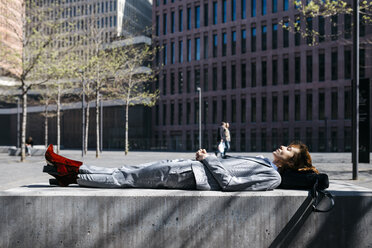 Junge Geschäftsfrau mit roten Schuhen, die sich auf einer Bank in der Stadt ausruht - JRFF03071