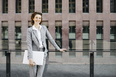 Businesswoman standing in he city, carrying laptop - JRFF03080