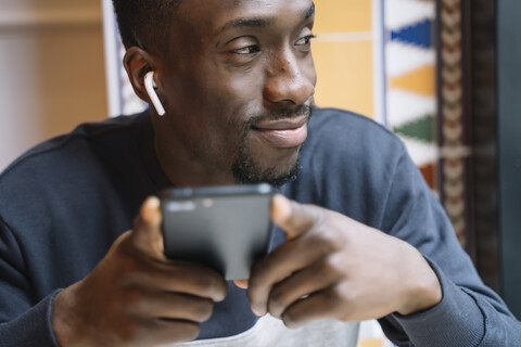 Lächelnder junger Mann mit drahtlosen Kopfhörern und Mobiltelefon, lizenzfreies Stockfoto