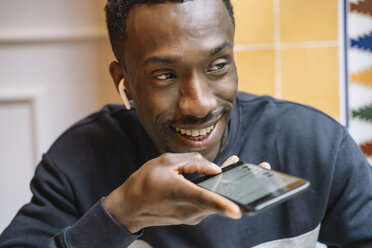 Porträt eines lächelnden jungen Mannes mit drahtlosen Kopfhörern am Telefon - OCMF00406