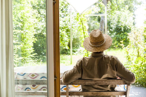 Back view of senior man wearing straw hat on terrace enjoying his garden - TCF06074