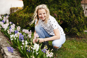 Young blonde woman controls hyacinths in her garden - HMEF00294