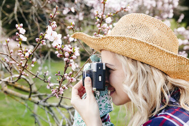 Junge Frau mit Strohhut fotografiert im Garten mit einer alten Kamera - HMEF00304