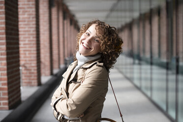 Portrait of happy woman with curly hair wearing beige trenchcoat and turtleneck pullover - EYAF00161