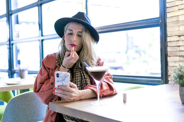 Frau hält Handy und trägt Lippenstift in einem Café auf - ERRF01072