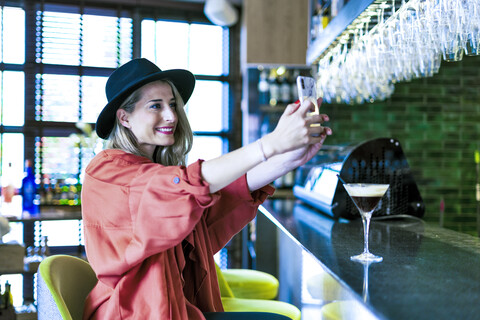 Lächelnde Frau, die an der Theke einer Bar sitzt und ein Selfie macht, lizenzfreies Stockfoto