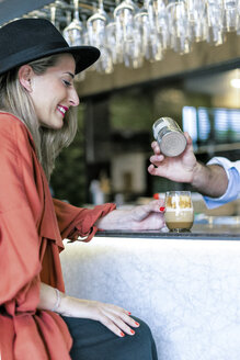 Lächelnde Frau am Tresen einer Bar, die den Barkeeper bei der Zubereitung eines Getränks beobachtet - ERRF01084