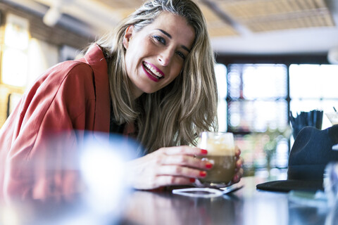 Porträt einer glücklichen Frau, die am Tresen einer Bar einen Drink zu sich nimmt, lizenzfreies Stockfoto
