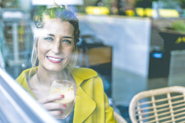 Portrait of smiling woman behind windowpane in a cafe - ERRF01097