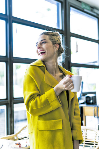 Glückliche Frau trinkt Kaffee am Fenster eines Cafés, lizenzfreies Stockfoto