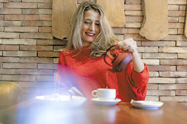 Smiling woman pouring tea into cup in a cafe - ERRF01112