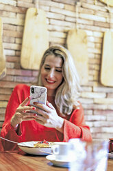 Lächelnde Frau benutzt Handy in einem Café - ERRF01114