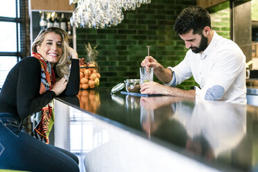 Smiling woman at the counter of a bar with barkeeper preparing a cocktail - ERRF01127