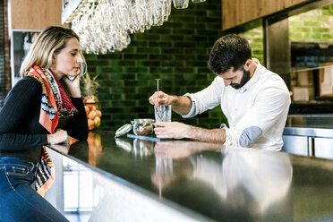 Frau mit Handy am Tresen einer Bar beobachtet Barkeeper bei der Zubereitung eines Cocktails - ERRF01128