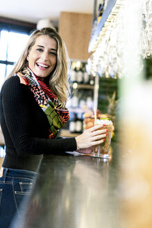 Porträt einer glücklichen Frau mit einem Cocktail an der Theke einer Bar - ERRF01134
