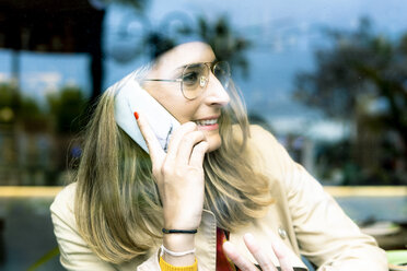Frau hinter Fensterscheibe telefoniert in einem Café - ERRF01138