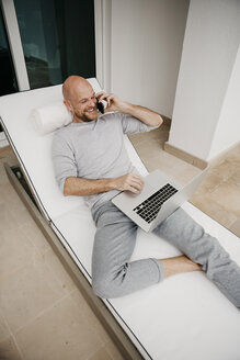 Glücklicher Mann auf dem Sofa liegend mit Handy und Laptop - LHPF00526