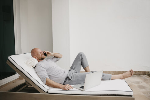 Glücklicher Mann auf dem Sofa liegend mit Handy und Laptop - LHPF00527