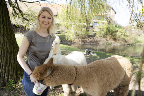 Porträt einer glücklichen Frau, die Alpakas füttert - FLLF00101