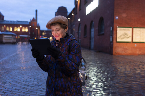 Deutschland, Berlin, Porträt eines lächelnden Touristen mit digitalem Tablet in der Dämmerung - TAMF01285