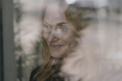 Lächelnde junge Frau hinter Fensterscheibe, lizenzfreies Stockfoto