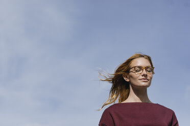 Porträt einer jungen Frau mit Brille und geschlossenen Augen unter blauem Himmel - GUSF01886