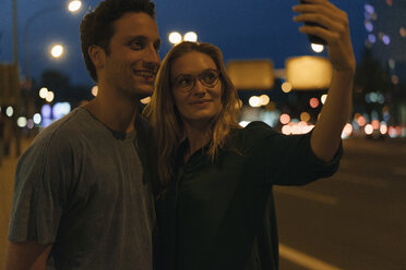 Lächelndes junges Paar macht ein Selfie in der Stadt bei Nacht - GUSF01898