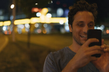 Happy young man using cell phone in the city at night - GUSF01903