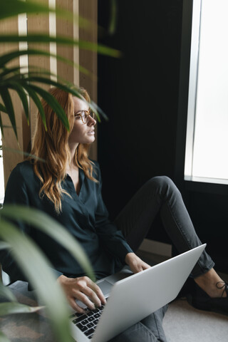 Geschäftsfrau sitzt auf dem Boden und benutzt einen Laptop, lizenzfreies Stockfoto