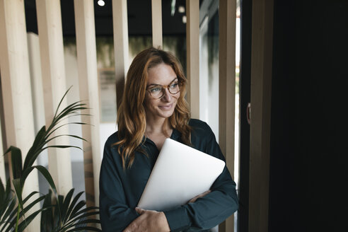 Lächelnde Geschäftsfrau mit Laptop und Blick zur Seite - GUSF01914