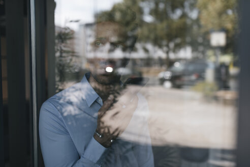 Junger Geschäftsmann hinter einer Fensterscheibe mit Mobiltelefon - GUSF01936