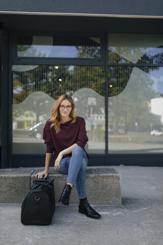 Portrait of young woman sitting outdoors with bag stock photo