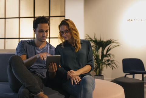 Young man and woman sitting on couch sharing tablet stock photo