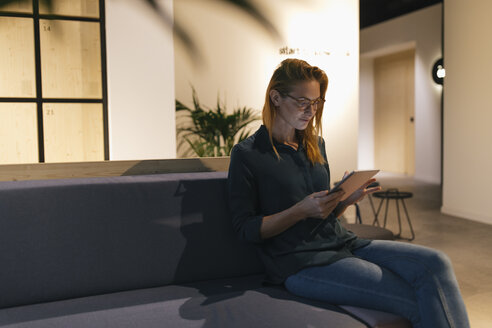 Geschäftsfrau sitzt auf der Couch und benutzt ein Tablet - GUSF01950