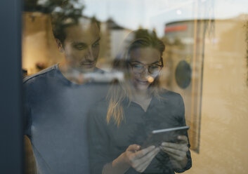 Young man and woman sharing tablet behind windowpane - GUSF01955