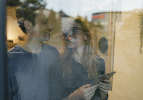 Smiling young man and woman with tablet behind windowpane stock photo