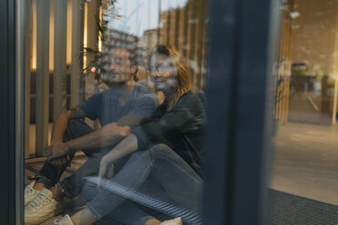 Junger Mann und Frau sitzen hinter einer Fensterscheibe und schauen hinaus - GUSF01958