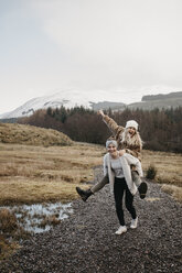 UK, Scotland, happy young woman carrying friend piggyback in rural landscape - LHPF00544