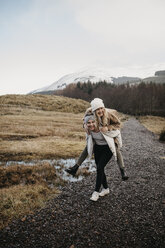 UK, Scotland, happy young woman carrying friend piggyback in rural landscape - LHPF00545