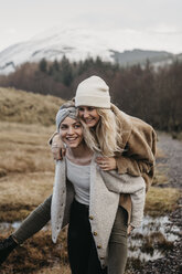 UK, Schottland, glückliche junge Frau, die ihren Freund huckepack trägt, in ländlicher Landschaft - LHPF00547